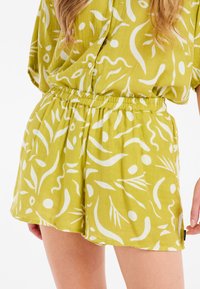 Pantaloni corti verdi con un motivo astratto bianco, dotati di cintura elasticizzata e vestibilità ampia, realizzati in tessuto leggero e traspirante.