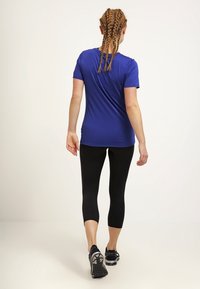 Korte mouwen, blauwe sporttop gecombineerd met zwarte capri-legging. De stof lijkt lichtgewicht en soepel, geschikt voor actieve kleding.