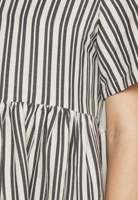 Vestido a rayas con líneas horizontales en negro y crema, con cintura fruncida y mangas cortas. Fabricado en una tela ligera con una textura suave.