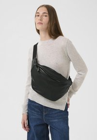 Borsa a tracolla in pelle nera con design curvo, dotata di tasca con zip e spallaccio regolabile. Texture liscia e stile minimalista.