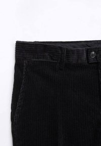 Gros plan sur la taille d'un pantalon en velours côtelé noir avec passants de ceinture, poche latérale et fermeture à bouton sur fond blanc.