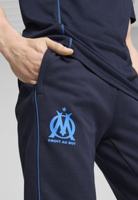 Jūrininkų jogger tipo kelnės pagamintos iš medvilnės blend, su mėlynais akcentais, šoninėmis kišenėmis ir ryšku mėlynu logotipu su tekstu "DROIT AU BUT."