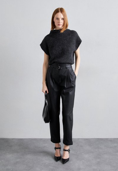 Μαύρη πλεκτή μπλούζα με ψηλό γιακά, συνδυασμένη με μαύρες ψηλόμεσες, πιέτα παντελόνες από δερματίνα και μαύρες γόβες με αιχμηρή μύτη. Κρατάει μια μαύρη τσάντα χεριού.