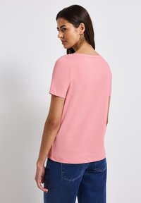 Kurzärmliges pinkes Baumwoll-T-Shirt mit rundem Ausschnitt und lockerer Passform, kombiniert mit dunkelblauen Jeans. Einfache, glatte Textur.