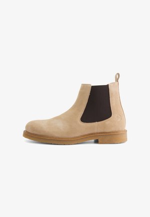 Beige suede Chelsea boot with elastic side panels, round toe, and a tan rubber sole. Features a pull tab at the back for easier wear.