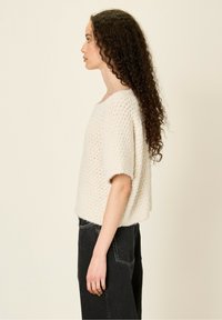 Pull en tricot texturé crème avec un col carré, des manches courtes et une coupe ample, associé à un jean noir taille haute.