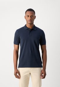 Marineblå polo skjorte i bomull med klassisk krage, korte ermer og en subtil logo på brystet. Slim fit med sidesplitter i kanten.