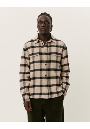 Beige en zwarte ruitjes flanellen shirt met twee borstzakken, knoopsluiting aan de voorkant en een kraag, gecombineerd met olijfgroene corduroypantalons.