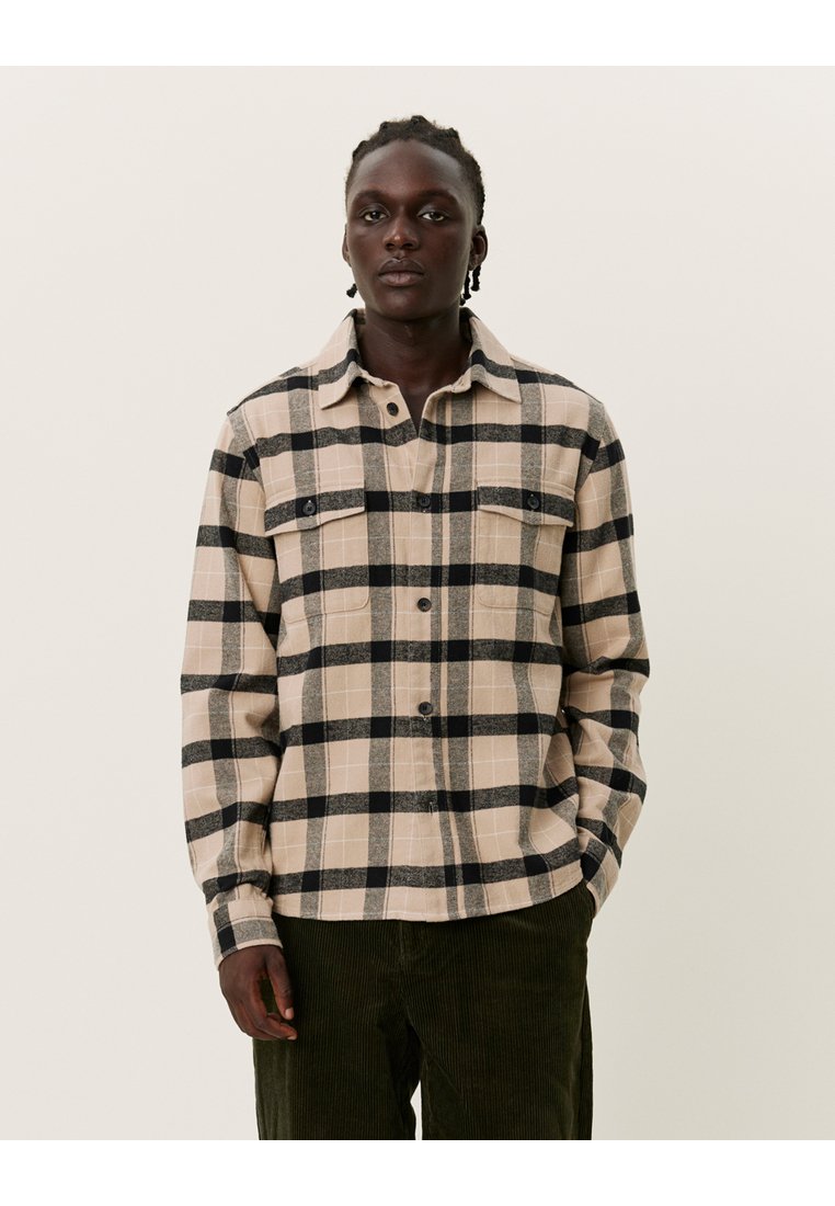 Beige en zwarte ruitjes flanellen shirt met twee borstzakken, knoopsluiting aan de voorkant en een kraag, gecombineerd met olijfgroene corduroypantalons.