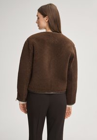 Brązowa, teksturowana kurtka o pudełkowym kroju i okrągłym dekolcie. Posiada długie rękawy, krótki fason oraz subtelne przeszycia z tyłu.
