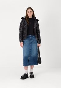 Black puffer jacket with a hood, paired with a dark sweater and denim skirt. Footwear: black platform clogs. Background: plain white.