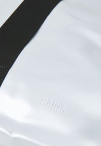 Hvitt vannavvisende stoff med en glatt tekstur, med en svart stropp og preget "RAINS"-logo, minimalistisk design.