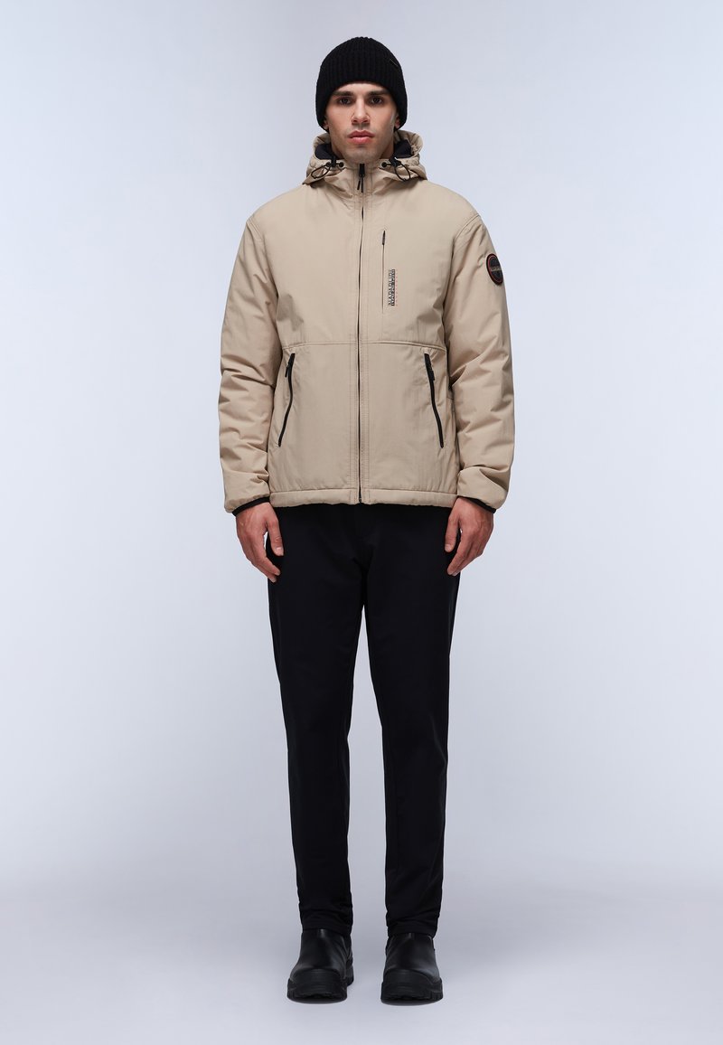 Beige geïsoleerde jas met een capuchon, rits aan de voorkant en twee zijzakken. Gekocht met zwarte broek en zwarte laarzen. Soepele textuur.