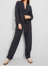 Černý oblek s propracovaným sako, které má zapínání na jediný knoflík, a kalhoty s širokými nohavicemi. Nosené s jasně barevnými teniskami.