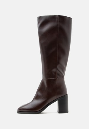 Botte haute en cuir marron foncé avec talon bloc et bout pointu sur fond blanc.