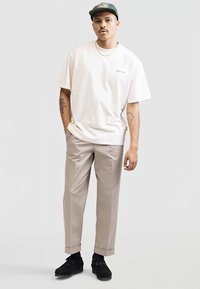 T-shirt en coton beige clair avec du texte vert, associé à un pantalon beige ajusté. Des chaussures noires à lacets complètent l'ensemble. Design simple, coupe décontractée.
