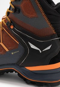 Botte de randonnée pour homme avec un design noir et orange, matériau Gore-Tex, surface texturée et semelle à traction multidirectionnelle.