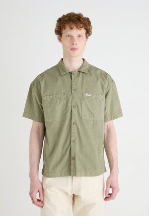 Short-sleeve olive green shirt made of cotton, featuring a button front, two chest pockets, and a label on the left pocket.