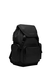 Sac à dos noir en tissu texturé avec des bretelles réglables, une fermeture à rabat, et deux poches zippées à l'avant pour le rangement.