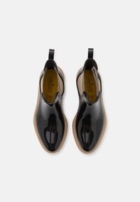 Botas negras brillantes hasta el tobillo con paneles laterales elásticos y tiradores. Suelas de goma color marrón claro. Interior con forro marrón claro y detalles de branding.