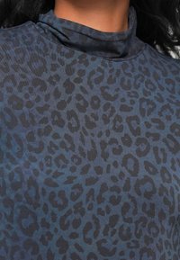 Langermet topp i mørkeblå stoff med et subtilt leopardmønster i varierende nyanser av blått og svart. Har høy hals.