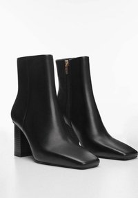 Botas de tobillo de cuero negro con punta cuadrada y tacón cuadrado, que cuentan con un zipper lateral y una textura suave y mate.