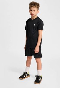 Svart atletisk t-shirt med korta ärmar och liten vit logotyp, kombinerad med svarta shorts, vita strumpor och svarta sneakers med gröna detaljer.