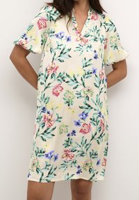 Květinové šaty z krémové látky s krátkými rukávy, které mají multicolor květiny a zelené listy v živém botanickém designu.