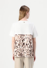 Biely tričko s leopardím vzorom na zadnej strane, s krátkymi rukávmi, okrúhlym výstrihom a malým zlatým akcentom na krku.