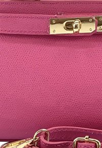 Roze leren tas met textuur, voorzien van een gouden sluiting en een bijpassende roze schouderband met gouden gesp, weergegeven in close-up.