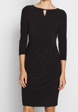 Schwarzes knielanges Kleid mit dreiviertel Ärmeln, mit Wickeldesign und einem kleinen silbernen Verschluss am Ausschnitt.