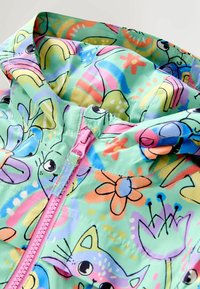 Värikäs kevyt takki, jossa mintunvihreä pohja ja leikkisiä piirrettyjä eläimiä, kukkia ja sateenkaaria. Huomionarvoinen vaaleanpunainen vetoketjutekijä.