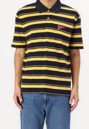 Polo rayé bleu marine et jaune en coton, avec un col classique et une petite écusson rouge sur la poitrine gauche.