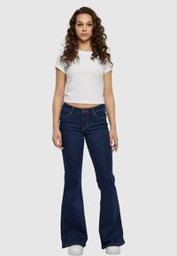 Donkerblauwe flared jeans met een vijf-pocket ontwerp, lichte stiksels en een aansluitende tailleband. Gepaard met een witte cropped top met korte mouwen.