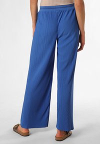 Blaue weit geschnittene Hose mit vertikalen Falten, elastischem Bund und glatter Textur, kombiniert mit braunen Sandalen und einem strukturierten Oberteil.