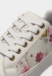 Baskets en cuir blanc avec lacets blancs, œillets dorés, détail triangulaire doré et motifs floraux roses sur le panneau latéral.