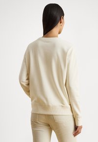 Φωτεινή μπεζ φούτερ κατασκευασμένη από απαλό ύφασμα, με στρογγυλή λαιμόκοψη, ριμπ τελειώματα στα μανίκια και το τελείωμα, καθώς και άνετη εφαρμογή. Ορατές ραφές.