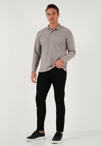 Långärmad grå polo med krage, i kombination med svarta slim-fit byxor och svarta sneakers med vita sulor. Slät textur överlag.