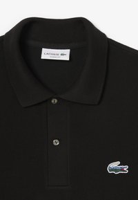Polo nero realizzato in tessuto testurizzato, con colletto classico, patta con due bottoni e un piccolo logo di coccodrillo ricamato.
