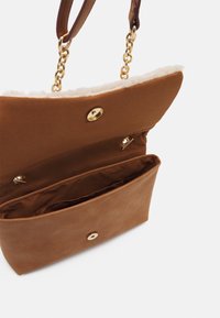 Braune Wildleder-Handtasche mit goldenen Beschlägen, ausgestattet mit einem flauschigen Innenfutter, einem Druckknopfverschluss und einer unterteilten Innentasche. Verstellbare Träger sind enthalten.