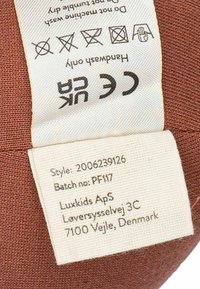 Étiquette en tissu marron avec des instructions d'entretien et des détails de marque. L'étiquette présente un bord texturé et un texte imprimé en noir sur un fond crème.