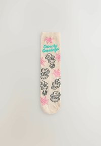 Ponožky po kolená béžovej farby s čiernymi ilustráciami Grincha a ružovými vzormi vločiek, s textom "Grinchy Greetings" v tyrkysovej farbe.