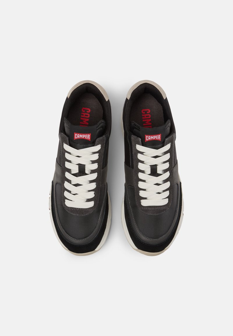 Zapatillas negras con cordones blancos y detalles en crema. Presentan una parte superior de cuero suave y una suela de goma robusta. Marca en la lengüeta.