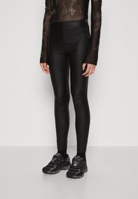 Fekete, magas derekú leggings sima textúrájú, fényes anyagból, fekete sportcipővel párosítva.
