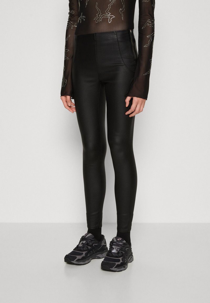 Fekete, magas derekú leggings sima textúrájú, fényes anyagból, fekete sportcipővel párosítva.