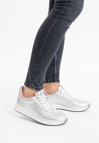 Zapatillas plateadas de cuero metálico, que presentan una suela blanca, diseño con cordones y acentos rosas en el talón, combinadas con jeans oscuros.