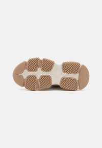 Shoe sole with a herringbone pattern in beige rubber, featuring circular and rectangular sections for traction and support.