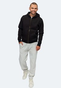 Schwarze Zip-Hoodie mit Fronttaschen, graue Jogginghosen und weiße Sneakers. Glatte Textur, lässige Passform, minimalistisches Design und keine sichtbaren Muster.