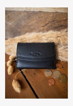 Mustast nahast rahakott tekstureeritud pinnaga ja õmmeldud detailidega, millel on reljeefne logo. Ümbritsetud müntide ja kuivatatud lilledega.