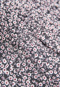 Tessuto nero con un piccolo motivo floreale in rosa e bianco. Il materiale ha una texture liscia con dettagli di cucitura arricciata.